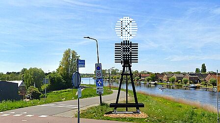 Baken met de K en P erop tussen het groen, de weg en het water.