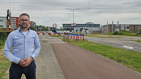 Rob Knijn staat met brede glimlach voor een spoorwegovergang in het Stationsgebied.